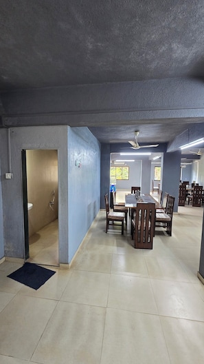Un espacio interior amplio con una larga mesa de comedor, sillas, dispensador de agua y un ventilador de techo.