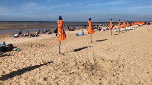 Ein Strand mit Reihen orangener Sonnenschirme und weißer Liegestühle.
