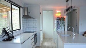 A modern kitchen with white cabinetry, a stainless steel range hood, a built-in oven, and a large window. - Coastal Retreat - 3 min walk to the beach 
Open for Monthly stays (Whangaparāoa)