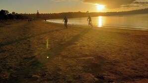A beach with people walking and cycling, a sunset in the background, and a calm sea. - Coastal Retreat - 3 min walk to the beach 
Open for Monthly stays (Whangaparāoa)