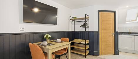 A dining area with a table, chairs, a TV, a shelf with shoes, and a door.