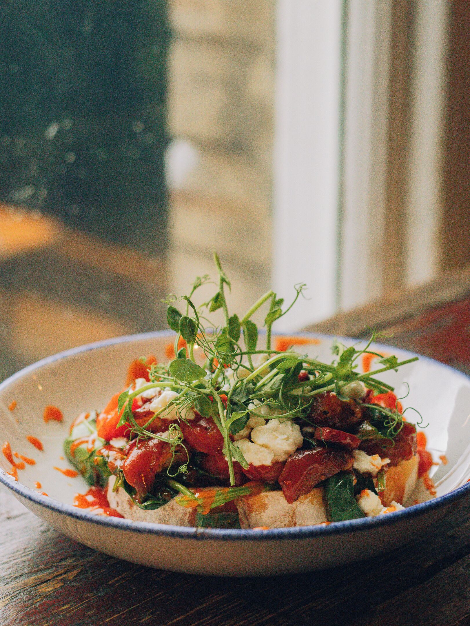 A bowl of food with greens, tomatoes, and cheese on a plate.