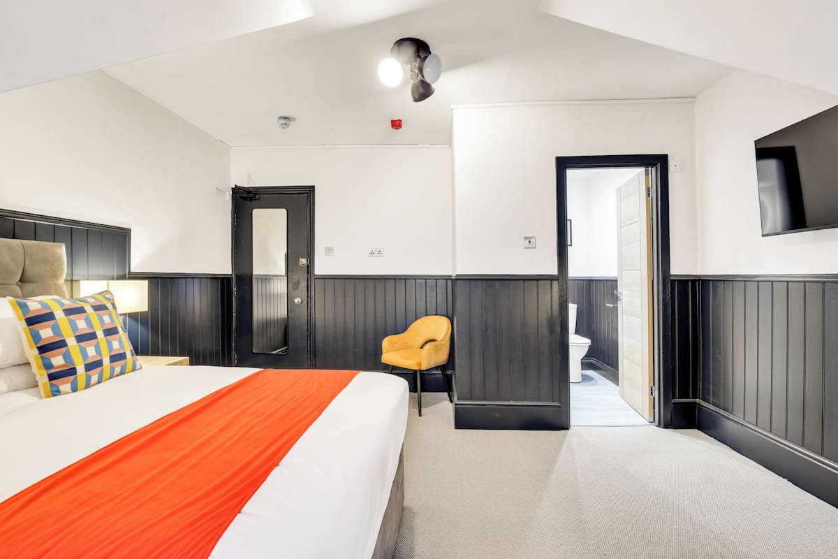 A hotel room with a bed, a chair, a TV, and a door leading to a bathroom.
