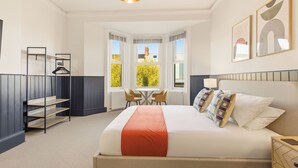 Una habitación de hotel con cama, mesa, sillas, ventana y lámpara colgante.