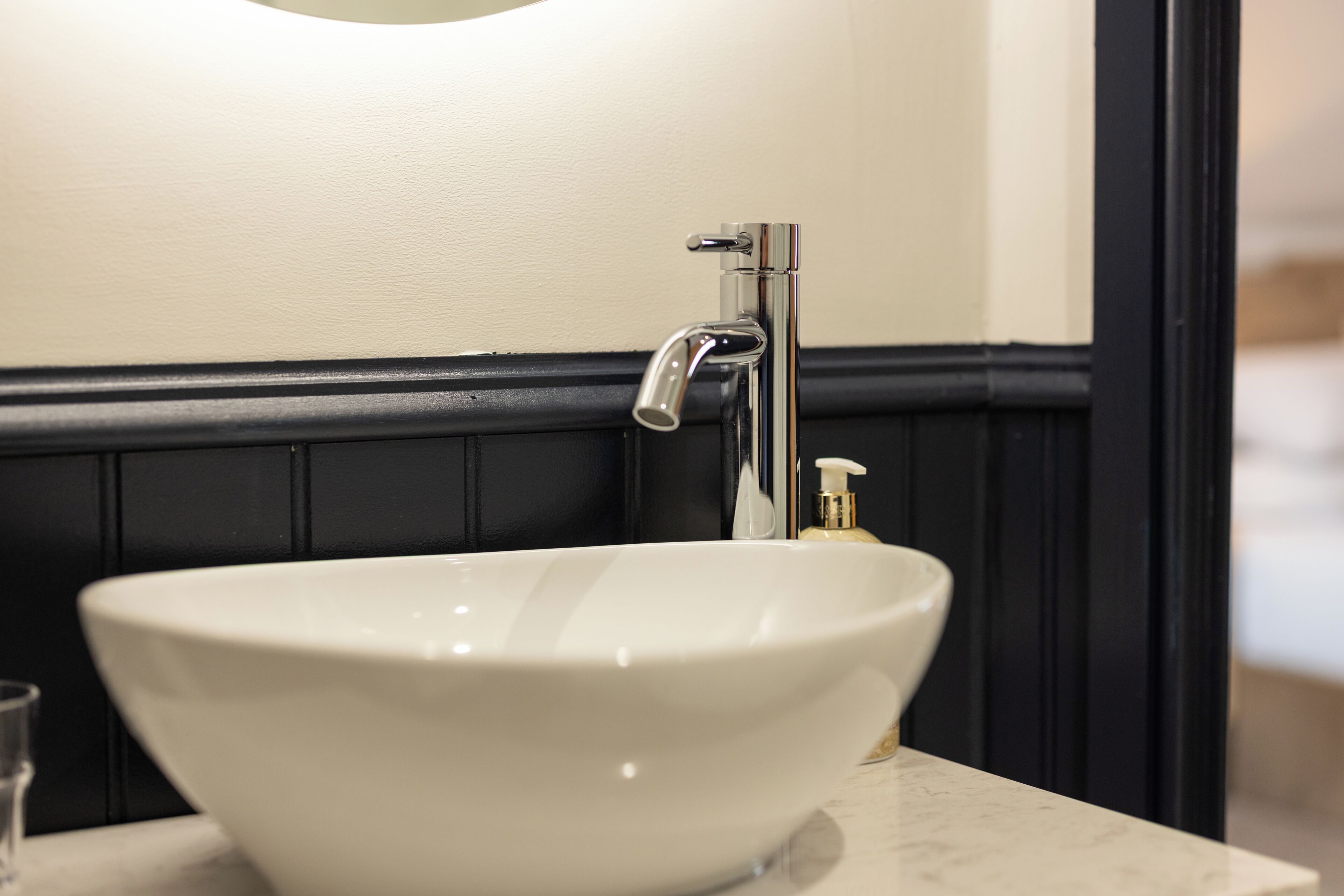A white vessel sink with a chrome faucet, a soap dispenser, and a glass on the countertop.