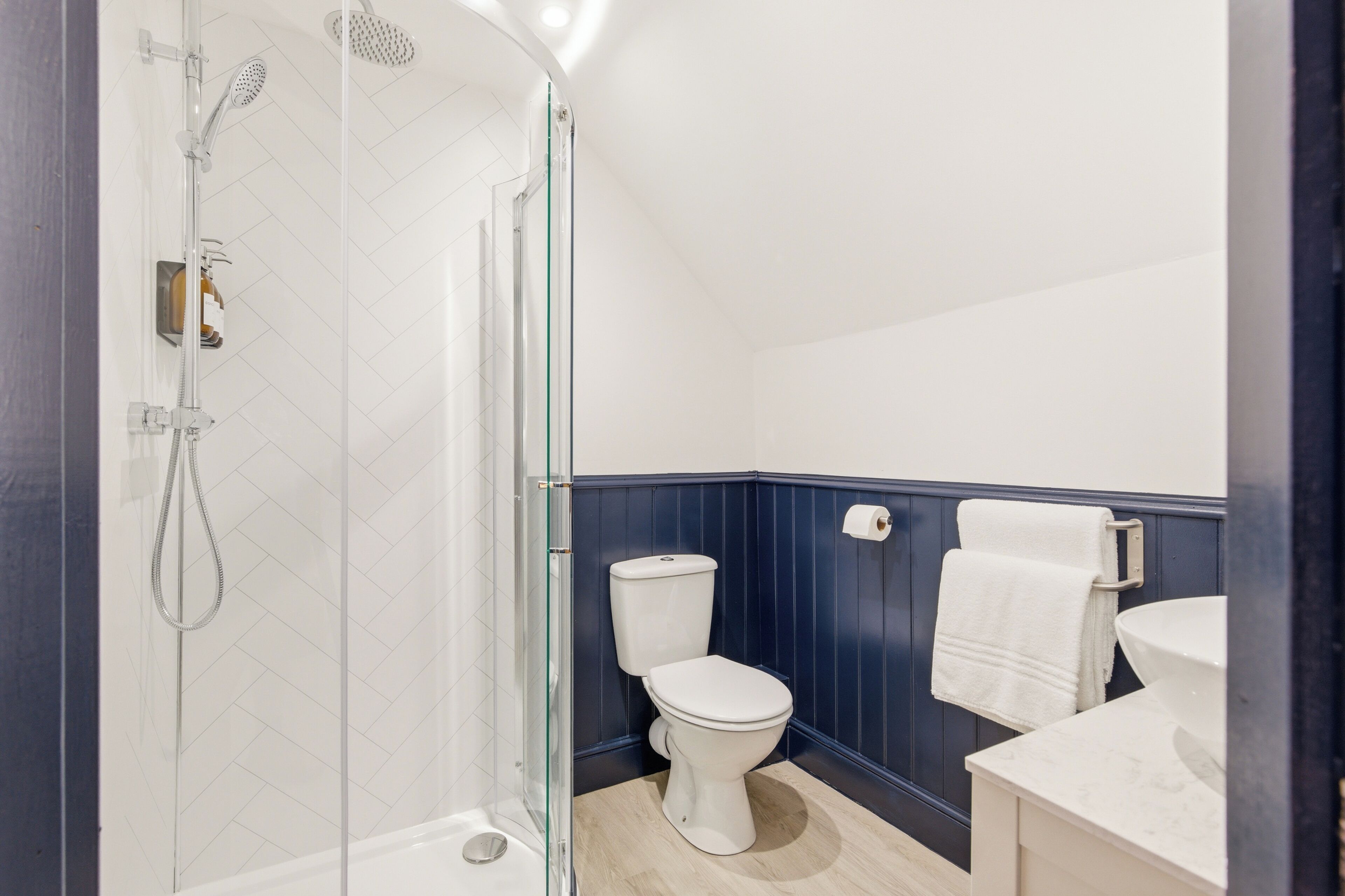 Un baño con ducha envuelta en vidrio, inodoro blanco y lavabo con toallero.