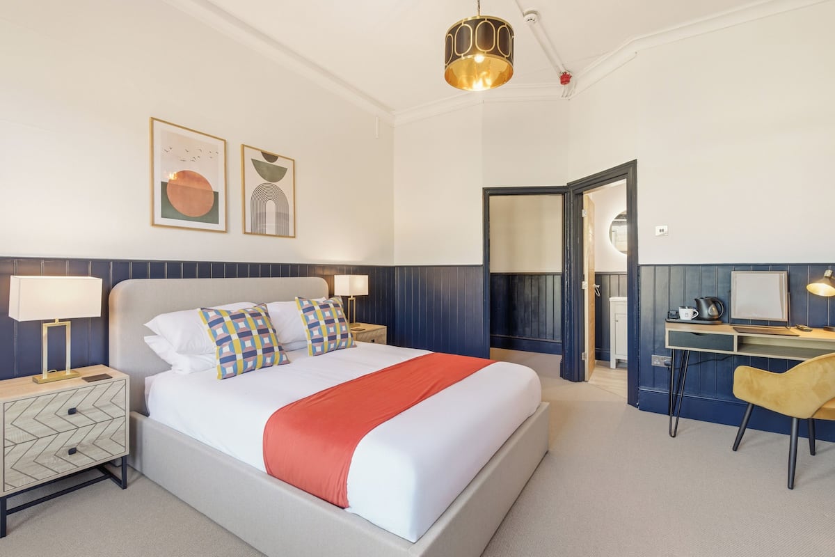 A hotel room with a bed, bedside tables, a desk, and a chair.
