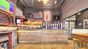 Un área de bar con suelo de madera, una barra con botellas y un letrero de neón.