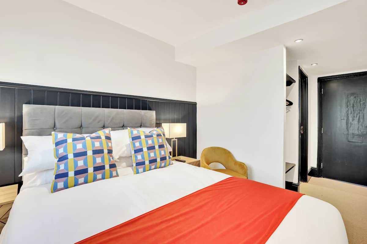 A hotel room with a large bed, a headboard, bedside lamps, a nightstand, and a door.
