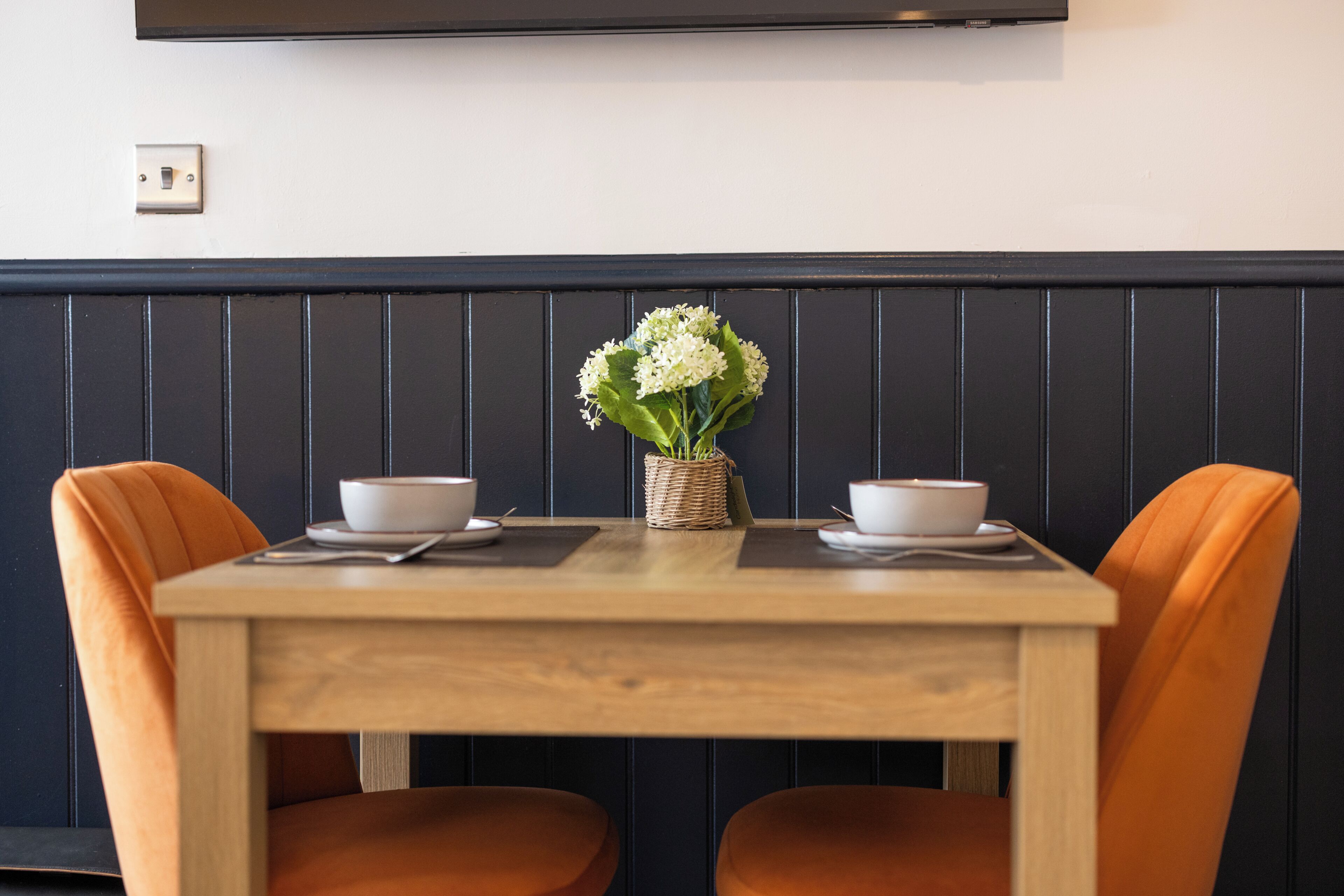 A dining table with two chairs, a vase with flowers, and a wall-mounted TV.