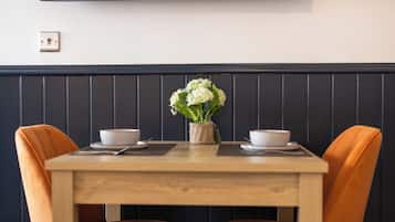 A dining table with two chairs, a vase with flowers, and a wall-mounted TV.