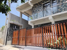 Um edifício moderno com entrada fechada por portão, varanda com guarda-corpo de vidro e uma placa indicando um negócio ou estabelecimento.