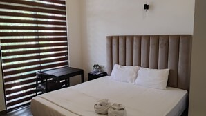 Une chambre d’hôtel avec un lit, une table de chevet, une petite table et une fenêtre avec des stores.