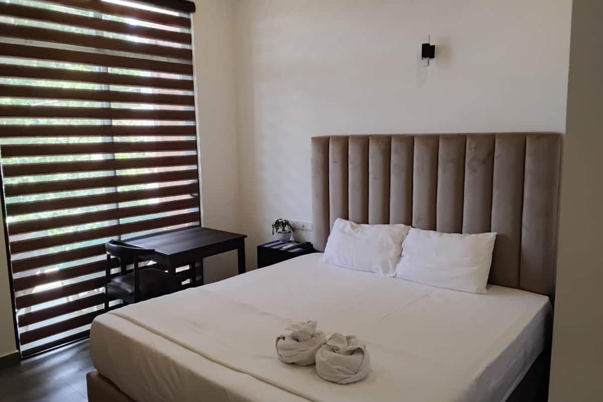 Een hotelkamer met een bed, nachtkastje, een klein tafeltje en een raam met jaloezieën.