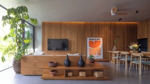 A modern reception area with a wooden reception desk, a flat-screen TV, a poster, and a dining area with wooden furniture. - Savara Villas Canggu (Canggu)