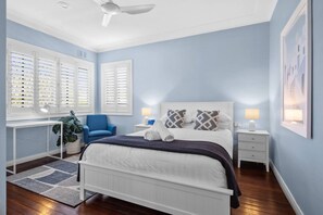 A bedroom with a bed, a desk, a chair, a plant, and a ceiling fan. - Endless Summer Sawtell - Luxe Beach Escape + Pool (Sawtell)