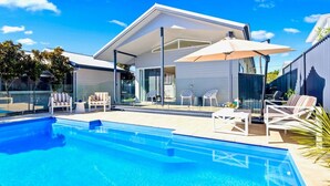 Une maison moderne dotée d’une piscine, d’un espace salon extérieur et d’un patio couvert.