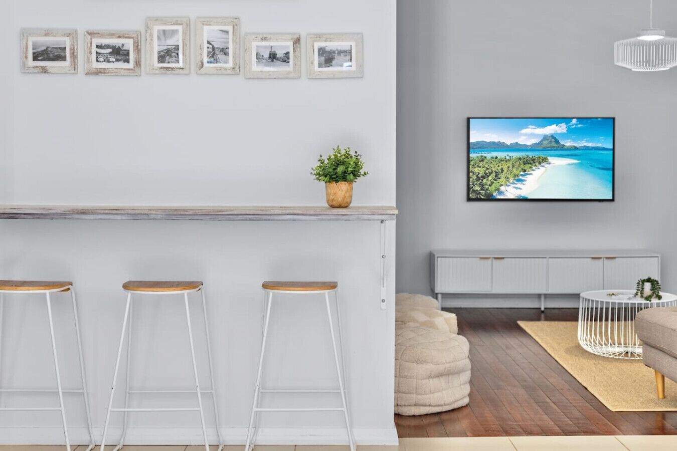 Un salon moderne doté d’un coin bar, de tabourets de bar blancs, d’un grand téléviseur à écran plat, d’une plante en pot et d’un espace salon confortable.