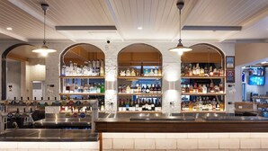 Un espace bar doté de plusieurs étagères remplies de bouteilles d’alcool, d’un comptoir et de luminaires suspendus.