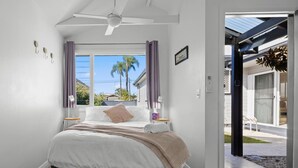 Une chambre à coucher avec un lit, un ventilateur de plafond, une fenêtre avec des rideaux et une vue sur l’extérieur.