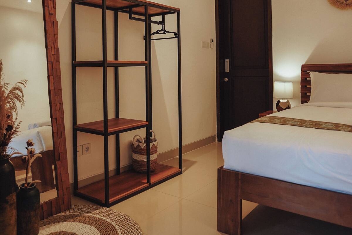 A bedroom with a bed, a wooden wardrobe, a mirror, and a small round rug.