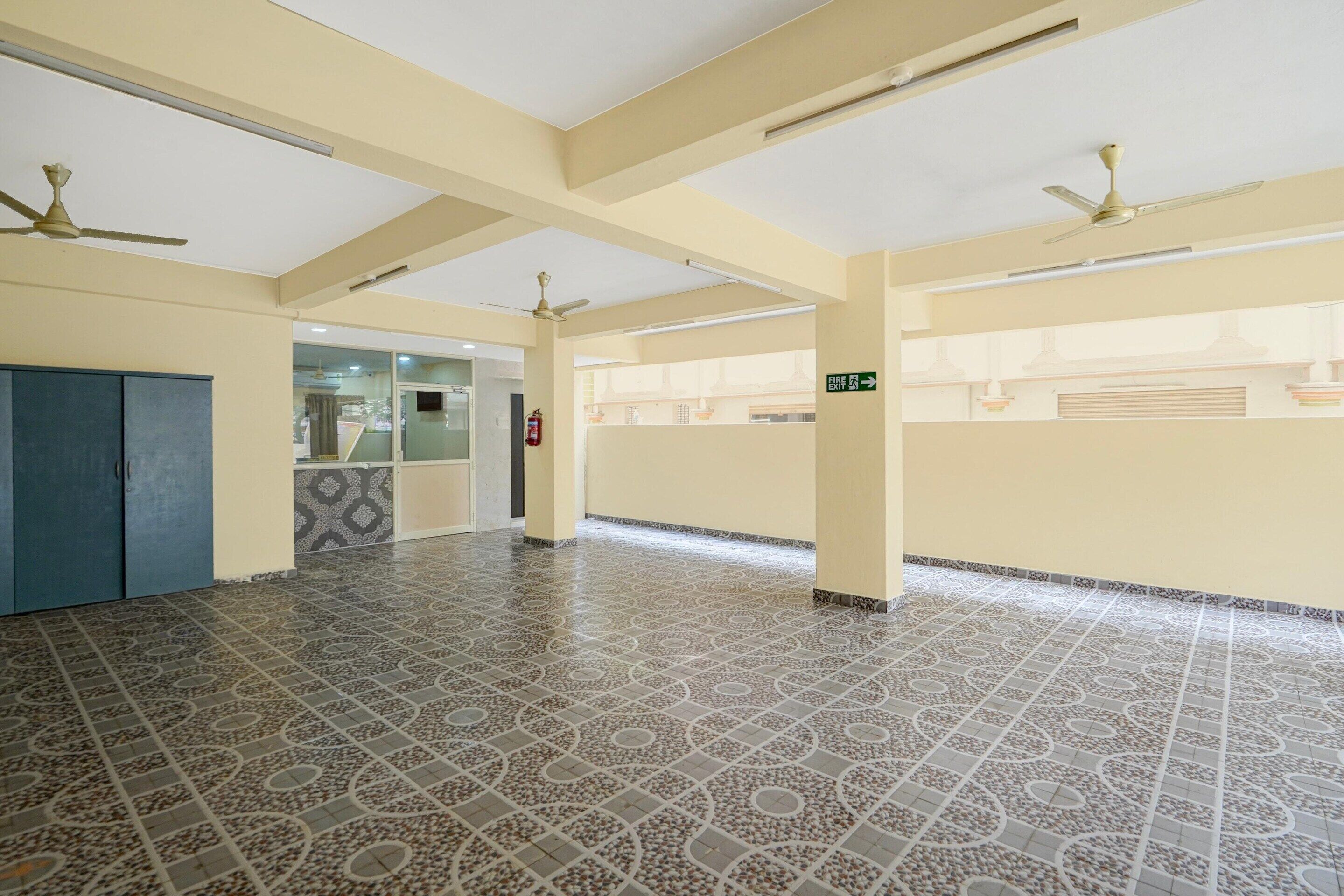 A spacious indoor area with patterned flooring, ceiling fans, and a visible exit sign.