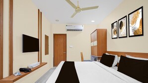 A hotel room with a bed, a TV, an air conditioner, a wooden desk, and artwork on the wall.