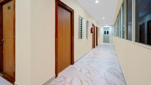 A corridor with wooden doors, windows with blinds, a fire extinguisher, and a marble floor.