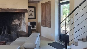 A living room with a sofa, a fireplace, a staircase, and a door leading outside. - House with spa in the heart of the countryside (Anglars-Nozac)