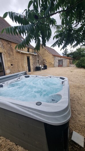 A hot tub in a backyard with stone buildings and a tree overhead. - House with a spa in the heart of the countryside (Anglars-Nozac)