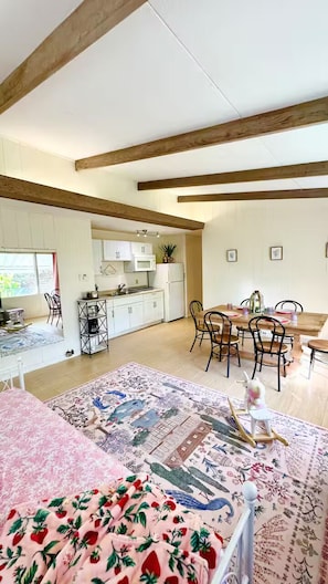A spacious living area with a dining table, chairs, a sofa, and a kitchen area with cabinets and appliances. - Oceanfront 2BR/2BA Home · 2 Kings, Fast WiFi, AC, BBQ & Fire Pit (Ewa Beach)