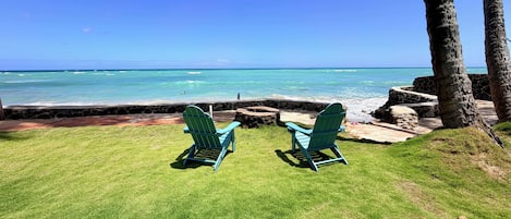 A grassy area with two green chairs facing a rocky shoreline and the ocean.