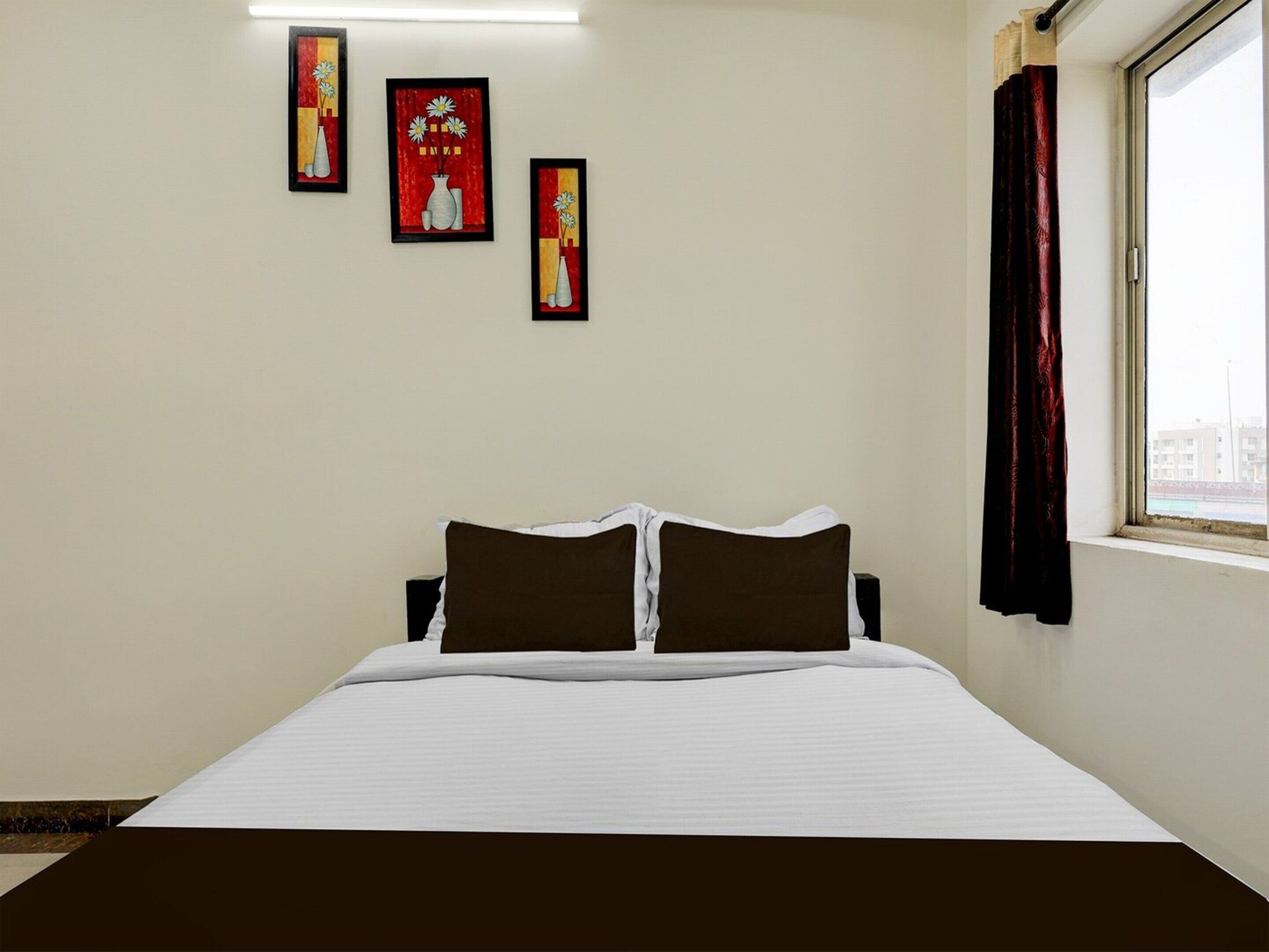 Ein Hotelzimmer mit Bett, Fenster mit Vorhängen und drei gerahmten Kunstwerken an der Wand.