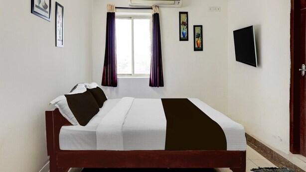A hotel room with a bed, a flat-screen TV, and a window with curtains.