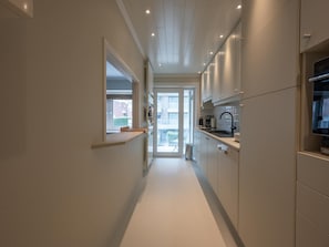 A modern kitchen with white cabinetry, a built-in oven, and a window overlooking a balcony. - Apartment in Knokke Near Albert Beach (Knokke-Heist)