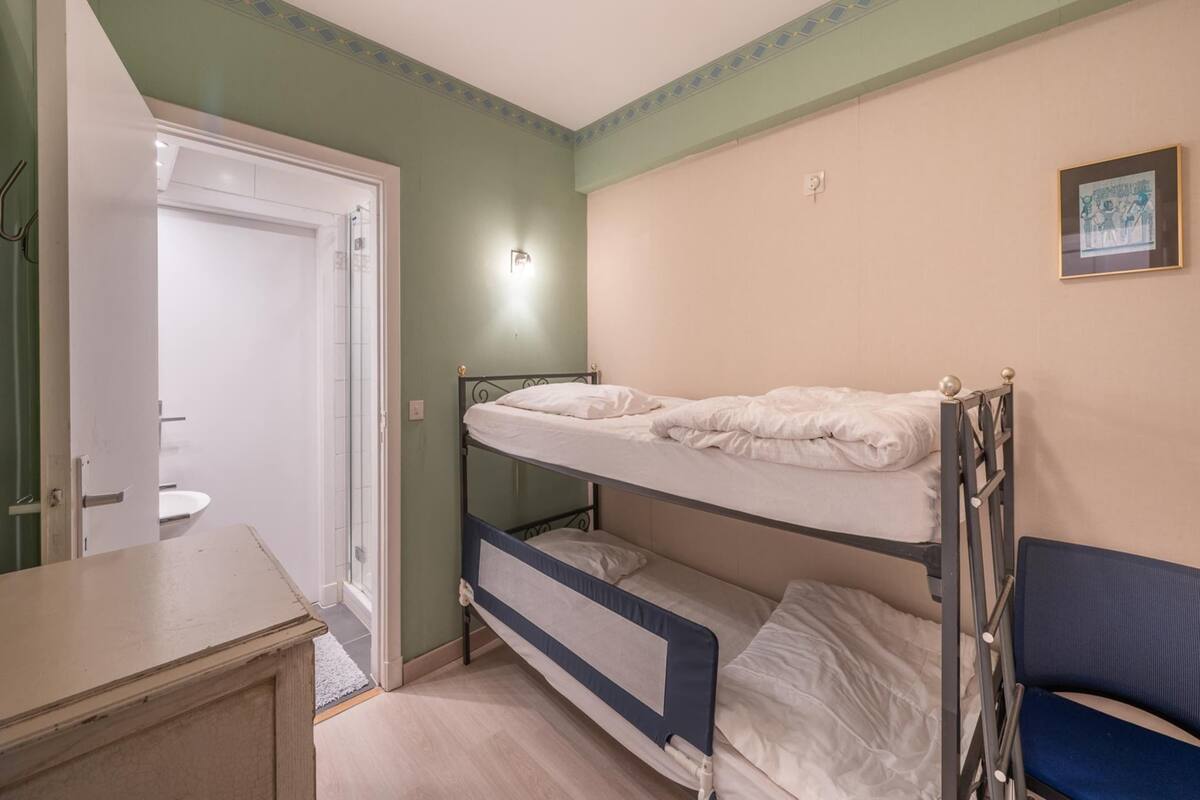 A bunk bed room with a door leading to a bathroom, a small desk, and a framed picture on the wall.
