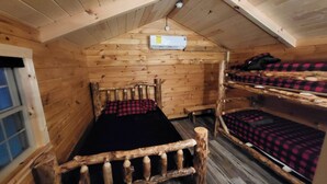 Una cabaña de madera con una cama nido, un ventanal y un equipo de aire acondicionado.
