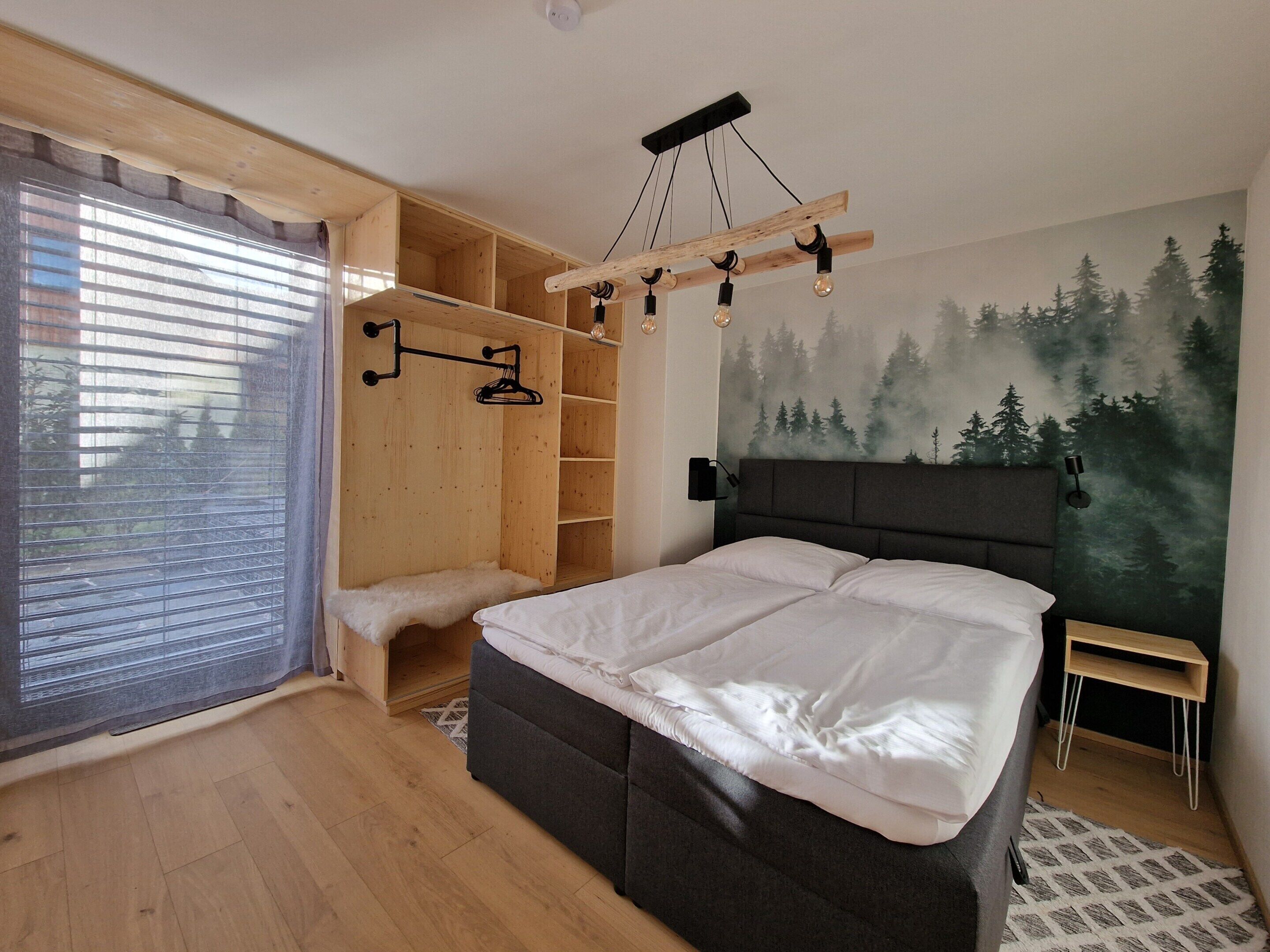 Ein Schlafzimmer mit einem Bett, einem Holzschrank, einer Bank und einer Waldmalerei an der Wand.
