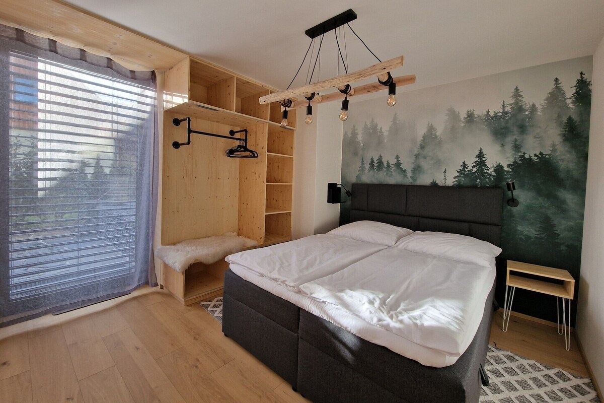 A bedroom with a bed, a wooden wardrobe, a bench, and a forest mural on the wall.