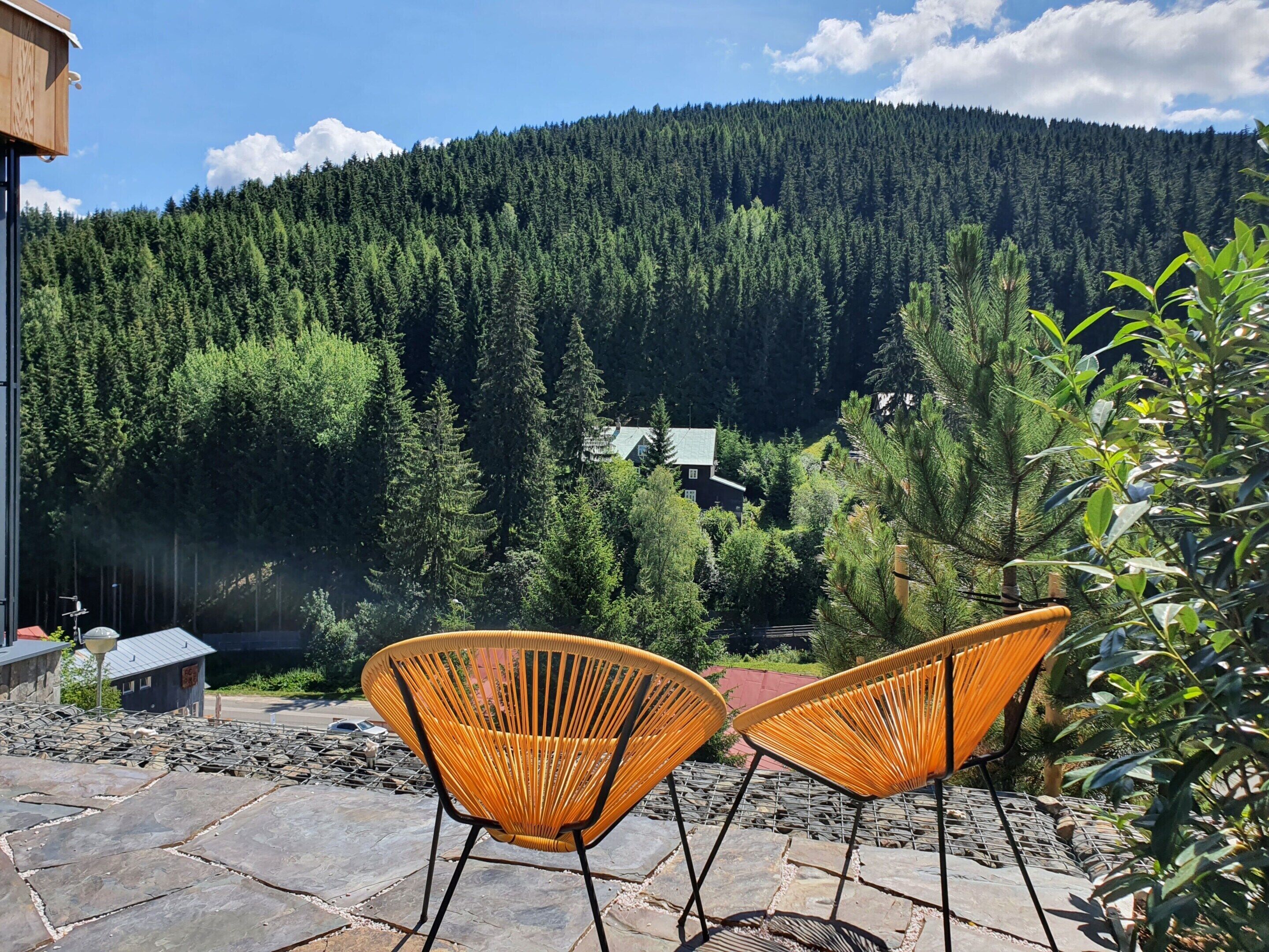 Eine Terrasse mit zwei Korbstühlen, Steinboden und Blick auf einen bewaldeten Berg.