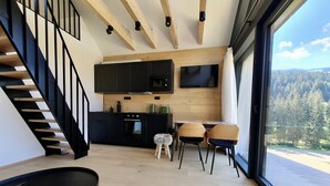 A modern kitchen with black cabinets, a wooden staircase, and a dining area with two chairs and a small stool. - Apartment in Krkonose With Mountain Views (Pec pod Snezkou)