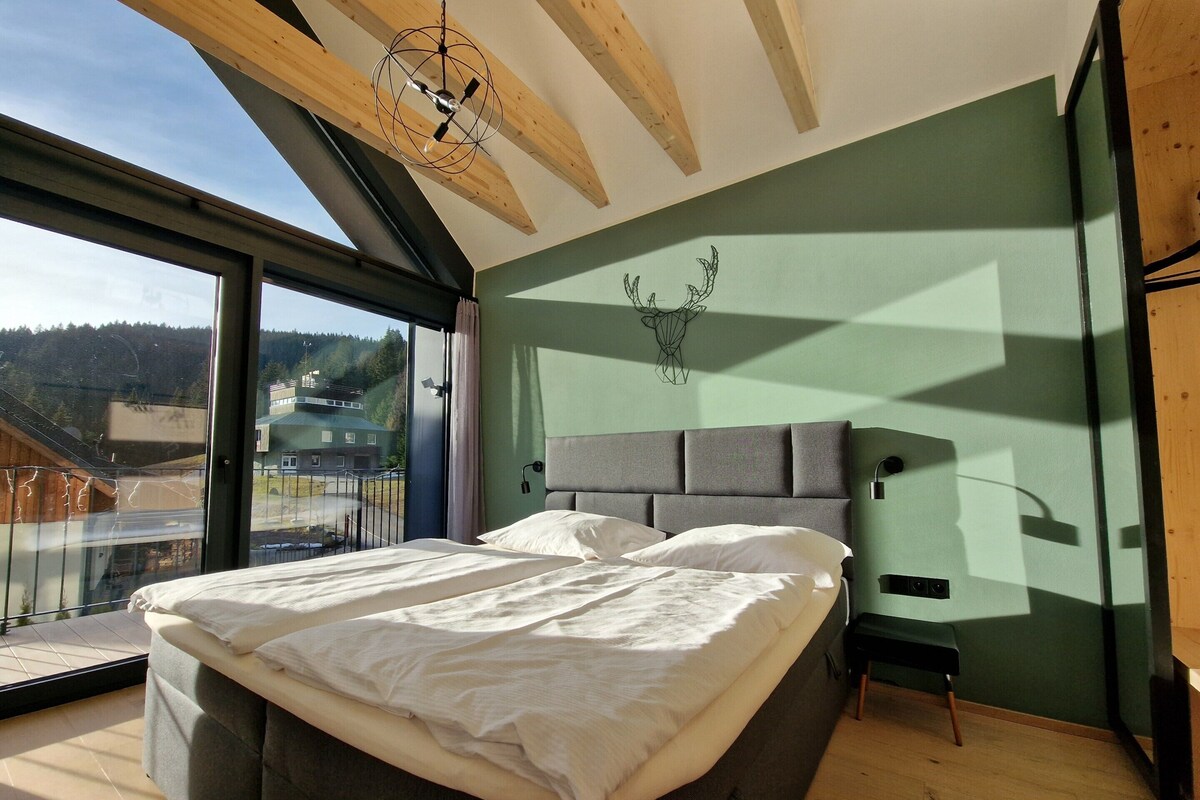 A modern bedroom with a large bed, a view of the outdoors, and a unique ceiling design.