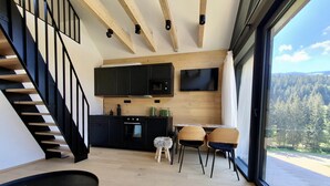 A modern kitchen with black cabinets, a wooden staircase, and a dining area with two chairs. - Apartment in Krkonose With Mountain Views (Pec pod Snezkou)