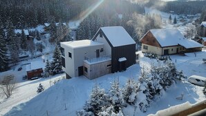 A modern two-story building with a flat roof and a small balcony, surrounded by snow-covered trees and a mountainous landscape. - Apartment in Krkonose With Mountain Views (Pec pod Snezkou)