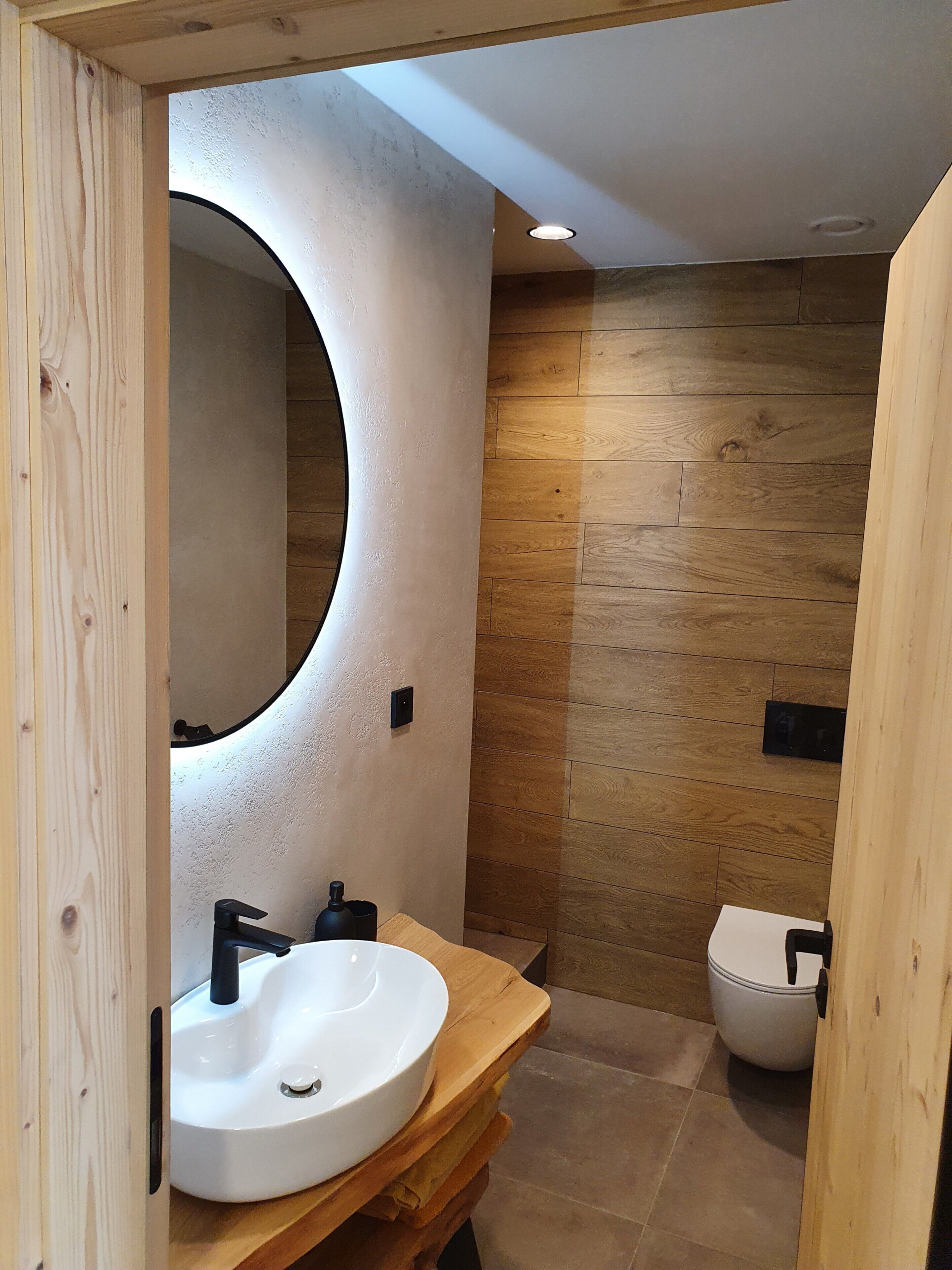 A modern bathroom with a wooden vanity, a round mirror, and a white sink.
