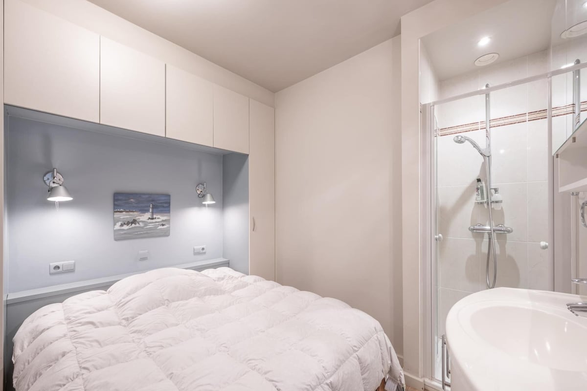A bedroom with a bed, a nightstand, a wall-mounted lamp, and a picture.