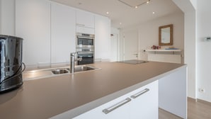 Une cuisine moderne dotée d’appareils électroménagers en acier inoxydable, d’un grand îlot central avec un évier et de meubles de cuisine blancs.