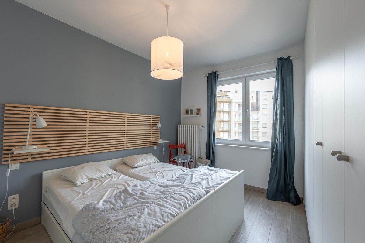 A bedroom with a bed, bedside lamps, a wooden slat headboard, a window with curtains, and a radiator.