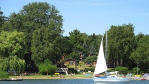 Una barca a vela su un lago, con un parco e degli edifici sullo sfondo.