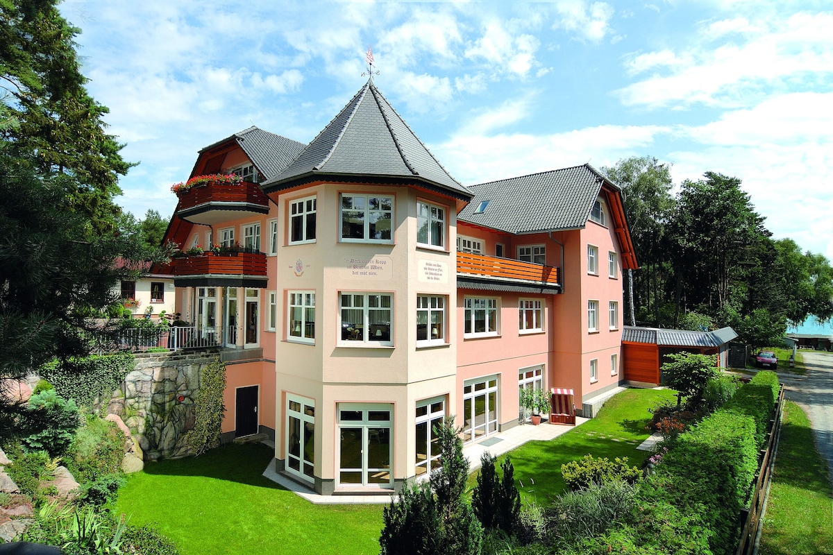 Ein mehrstöckiges Gebäude mit einem markanten Turm, großen Fenstern und einem gepflegten Garten.
